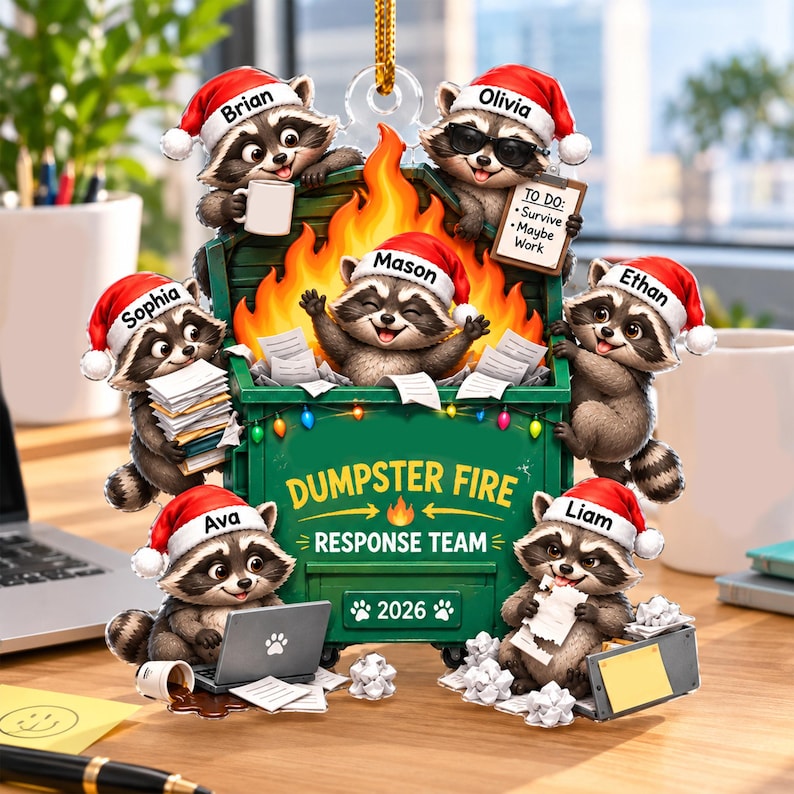 May include: A decorative ornament featuring six raccoons wearing Santa hats around a green dumpster filled with flames. The dumpster is labeled DUMPSTER FIRE RESPONSE TEAM 2026. Each raccoon is personalized with names: Brian, Olivia, Mason, Sophia, Ethan, Ava, and Liam.