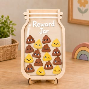 May include: A light-colored wooden reward jar with a clear acrylic front panel featuring the white text "Reward Jar". Inside the jar are several small, flat, cartoon-style poop-shaped tokens in shades of brown and yellow with smiling faces.
