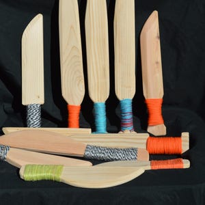 May include: A collection of wooden kitchen utensils, including spatulas and knives, with natural wood tones. The handles are wrapped with colorful twine in shades of orange, blue, green, and black and white.