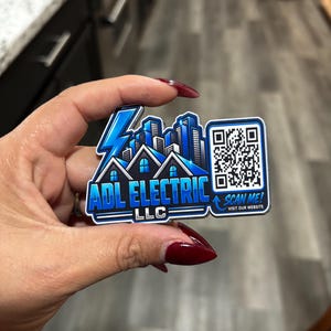 May include: A custom shaped sign featuring a blue lightning bolt, a city skyline, and a house silhouette. The text reads ADL ELECTRIC LLC. A QR code is on the right side with the text SCAN ME! VISIT OUR WEBSITE printed in blue below the code.