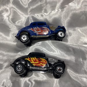 May include: Two toy hot rod cars with flames painted on the sides. One car is blue and the other is black.