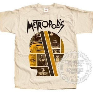 Puede incluir: Una camiseta beige con un gráfico negro y amarillo de una cabeza compuesta por fotogramas de la película "Metropolis". El texto "Metropolis" está en negro y amarillo y el texto "A Film By Fritz Lang" está en negro y blanco.