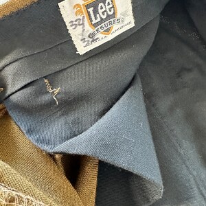 May include: A brown pair of Lee  'Lee-sures' pants with a black waistband and a white tag that says 'Lee' and 'Lee-sures' with the size '34' written in black marker.