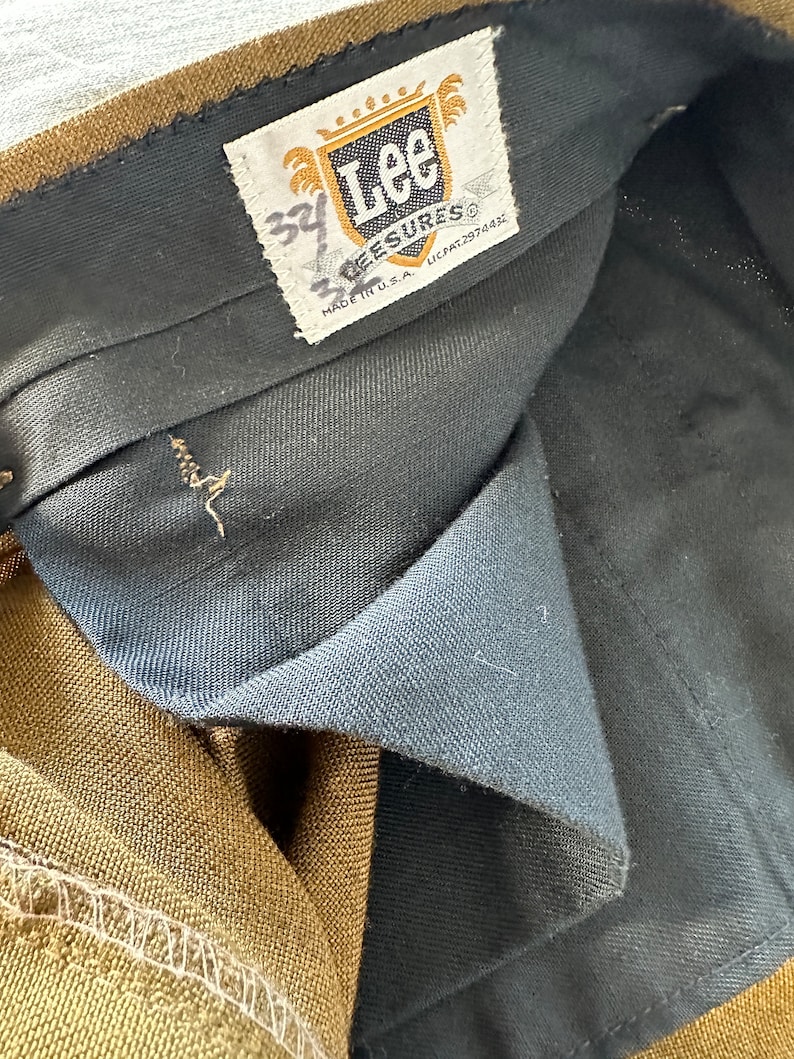 May include: A brown pair of Lee  'Lee-sures' pants with a black waistband and a white tag that says 'Lee' and 'Lee-sures' with the size '34' written in black marker.