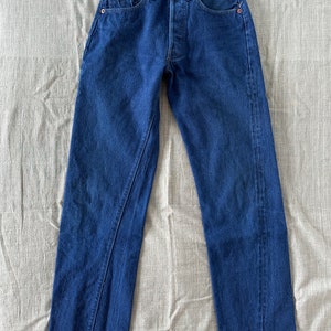 May include: A pair of dark blue denim jeans with a classic five-pocket style. The jeans have a straight leg and a button fly.