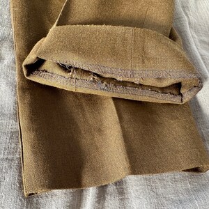 May include: Close-up of the hem of a pair of brown pants. The hem is folded over and sewn with a dark thread. The fabric is a woven twill.
