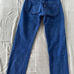 May include: A pair of dark blue denim jeans with a red leather patch on the back waistband. The jeans have a classic straight leg fit.