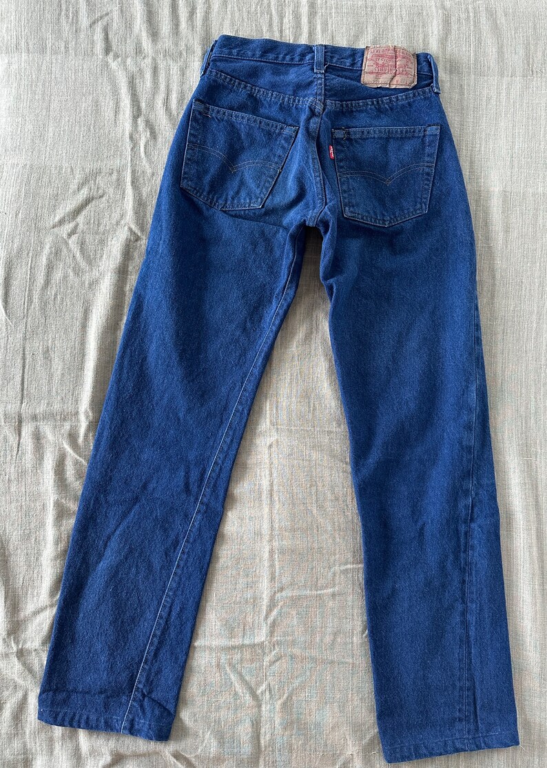 May include: A pair of dark blue denim jeans with a red leather patch on the back waistband. The jeans have a classic straight leg fit.