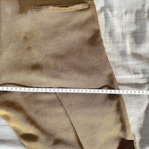May include: Close-up of a pair of brown pants with a pocket on the back. A measuring tape is laid across the pants, showing a measurement of 70 inches.