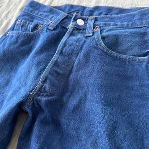May include: A pair of dark blue denim jeans with a classic five-pocket style. The jeans have a straight leg and a button fly.