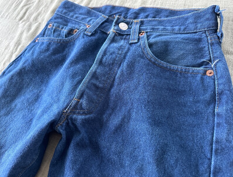 May include: A pair of dark blue denim jeans with a classic five-pocket style. The jeans have a straight leg and a button fly.