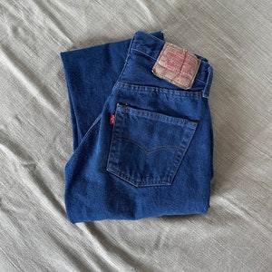 May include: A pair of blue denim jeans folded in half, with a brown Levi's label on the back pocket. The label has the text "Levi Strauss & Co.", "San Francisco, Cal.", "Original  Quality  Clothing", "W 31 L 32", and "501".