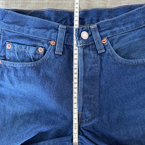 May include: A close-up of a pair of blue denim jeans with a measuring tape placed vertically along the center seam. The tape measures 35 inches.