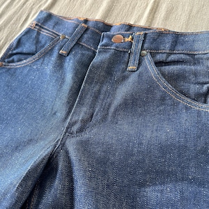 Op de afbeelding: Close-up van een donkerblauwe denim jeans. De jeans heeft een klassiek ontwerp met vijf zakken, koperkleurige klinknagels en stiksels. De stof heeft een licht versleten uiterlijk, wat wijst op een vintage of geliefd item.