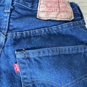 May include: A pair of blue denim jeans with a Levi's label on the back pocket. The label reads "Levi Strauss & Co. Original Quality Clothing" and has the size "W 27 L 32" printed on it.