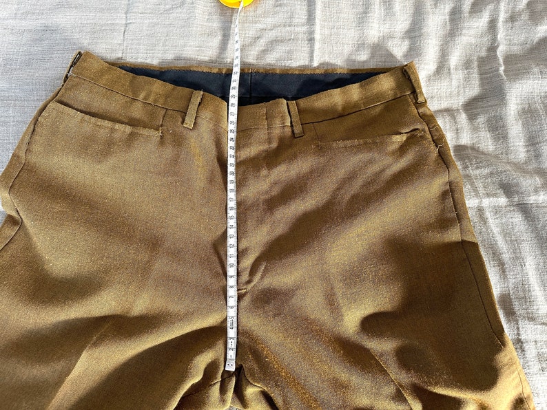 May include: A pair of brown pants with a black waistband and a measuring tape running down the center.