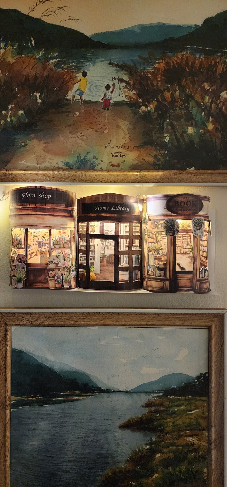May include: Three papercraft shop fronts with lights. The shops are a flora shop, a home library, and a book shop. Each shop has a window with a view inside. The shops are on a white background.