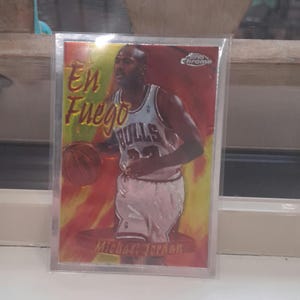 Könnte beinhalten: Eine Basketballkarte von Michael Jordan in einer Schutzhülle. Die Karte zeigt Jordan im Chicago Bulls-Trikot, der einen Basketball hält. Die Worte "En Fuego" und "Michael Jordan" sind auf die Karte gedruckt.