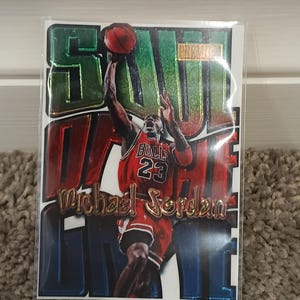 May include: A basketball trading card featuring Michael Jordan in a red Chicago Bulls uniform, mid-air with the ball. The card has a glossy finish with the words "Soul Game" and "Michael Jordan" in gold lettering.