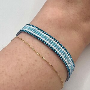 May include: A blue and white beaded bracelet with a gold chain bracelet on a person's wrist.