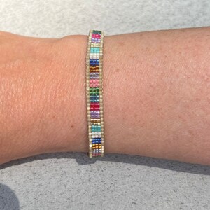 May include: A colourful beaded bracelet with a white base and a variety of coloured beads, including pink, blue, green, and gold.