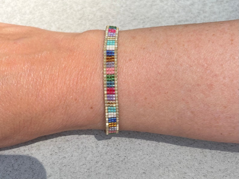 May include: A colourful beaded bracelet with a white base and a variety of coloured beads, including pink, blue, green, and gold.