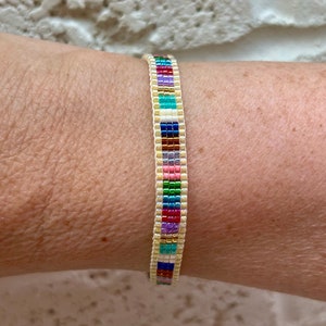 May include: A colourful beaded bracelet with a white base and a variety of colours including red, orange, yellow, green, blue, purple, and pink.