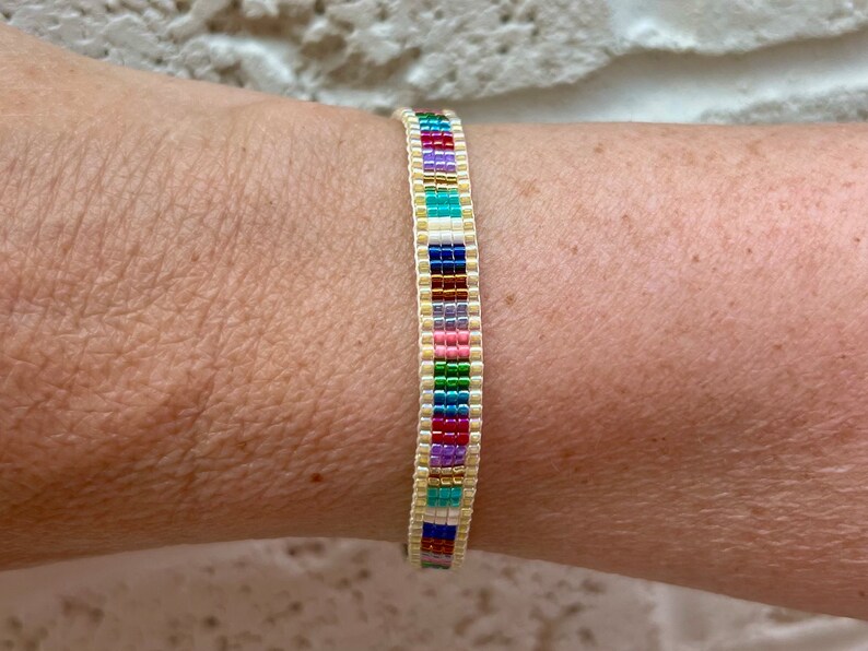 May include: A colourful beaded bracelet with a white base and a variety of colours including red, orange, yellow, green, blue, purple, and pink.