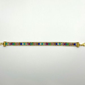 May include: A gold beaded bracelet with a colourful geometric pattern. The bracelet has a clasp closure.