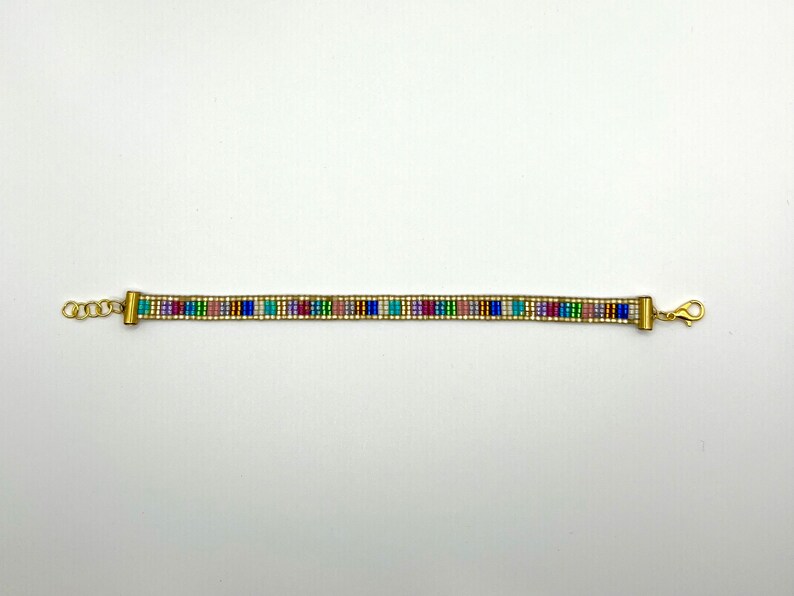 May include: A gold beaded bracelet with a colourful geometric pattern. The bracelet has a clasp closure.