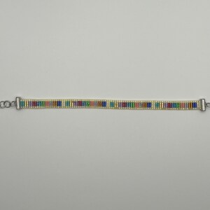 May include: A beaded bracelet with a silver clasp and a colourful striped pattern. The bracelet is made with small, white beads and colourful beads in shades of blue, green, pink, and yellow.