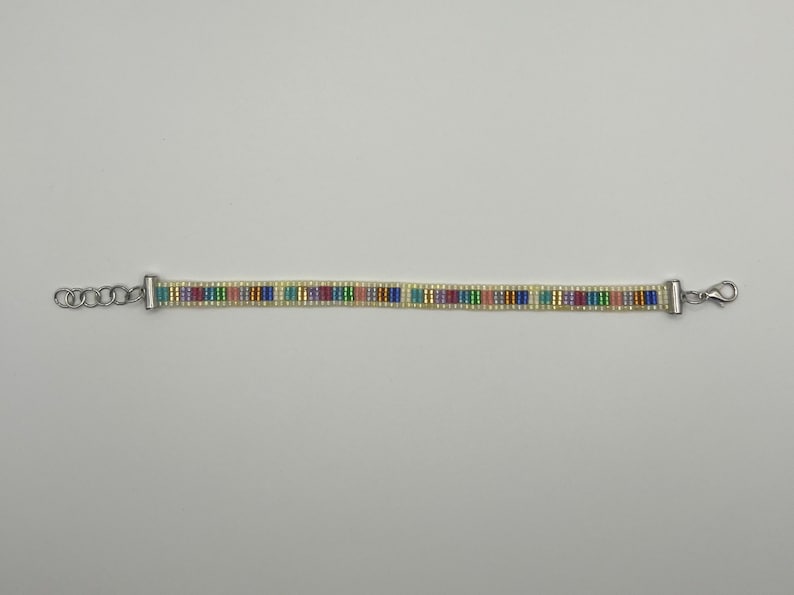 May include: A beaded bracelet with a silver clasp and a colourful striped pattern. The bracelet is made with small, white beads and colourful beads in shades of blue, green, pink, and yellow.