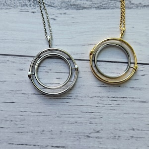 May include: Two necklaces with circular pendants. One necklace has a silver pendant with a double circle design. The other necklace has a gold pendant with a double circle design.