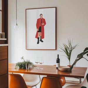 Könnte beinhalten: Ein gerahmter Kunstdruck mit einer stilisierten Illustration einer Person in einem roten Mantel, schwarzen Shorts und Stiefeln. Das Kunstwerk hängt an einer weißen Wand über einem Holzesstisch mit orangefarbenen Stühlen. Auf dem Tisch stehen eine Weinflasche und Gläser.