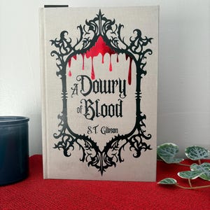 Può includere: Un libro intitolato "A Dowry of Blood" di S.T. Gibson. La copertina presenta una cornice nera ornata con una sostanza rossa simile al sangue che cola dall'alto.