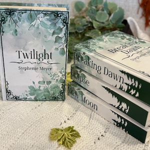 May include: A set of Stephenie Meyer's "Twilight" books. The covers are white with green and blue watercolour foliage designs. The titles "Twilight", "Breaking Dawn", "Eclipse", and "New Moon" are displayed on the spines.