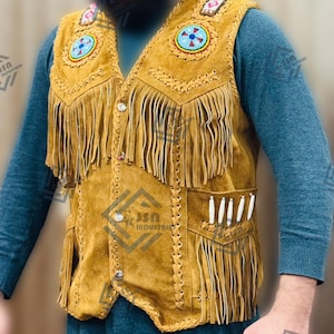 May include: A brown suede waistcoat with fringe and beaded designs. The waistcoat has a zip fastening and two pockets. The waistcoat is decorated with white bone accents.