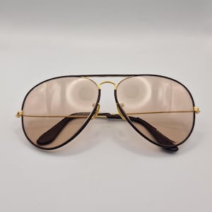 K&ouml;nnte beinhalten: Sonnenbrille im Aviator-Stil mit einem goldfarbenen Metallrahmen und braunen Gl&auml;sern. Die Sonnenbrille hat einen Doppelsteg und dunkelbraune B&uuml;gel. Die Gl&auml;ser sind hellbraun.