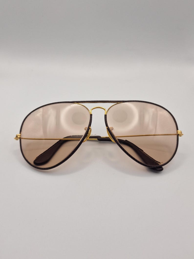 K&ouml;nnte beinhalten: Sonnenbrille im Aviator-Stil mit einem goldfarbenen Metallrahmen und braunen Gl&auml;sern. Die Sonnenbrille hat einen Doppelsteg und dunkelbraune B&uuml;gel. Die Gl&auml;ser sind hellbraun.