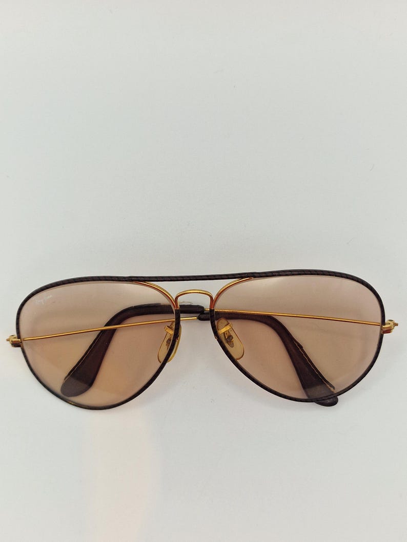 K&ouml;nnte beinhalten: Aviator-Sonnenbrille mit goldfarbenem Metallrahmen und braunen Gl&auml;sern. Die Sonnenbrille hat eine klassische Tropfenform und dunkelbraune Akzente an den B&uuml;geln und am oberen Rahmen. Die Gl&auml;ser sind hellbraun.