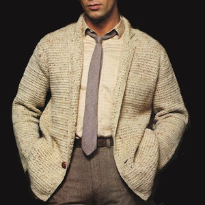 May include: A beige crochet jacket with a brown button, worn over a light-colored shirt and a gray tie. The jacket has pockets and is paired with brown trousers. The overall look is classic and stylish.