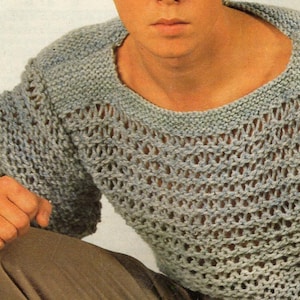 Puede incluir: Un suéter gris claro de tejido abierto, con cuello redondo y mangas largas. El diseño de punto presenta un patrón texturizado con secciones abiertas. Las mangas tienen una apariencia ligeramente abullonada. El suéter está hecho de un material suave, posiblemente lana.