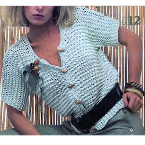 Puede incluir: Un cárdigan de punto azul claro con cuello en V y botones de madera. El cárdigan tiene mangas cortas y se lleva con un cinturón negro y pantalones marrones.