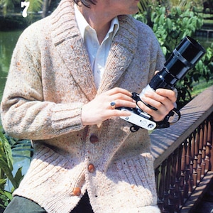 Op de afbeelding: Een beige cardigan met een shawlkraag en knoopsluiting. De cardigan heeft een gespikkeld patroon en is gemaakt van een zachte, gebreide stof.