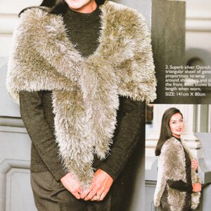 May include: A silver ostrich feather shawl with a triangular design. The shawl is worn over a dark grey long-sleeve top and dark trousers. The shawl measures 141cm long by 80cm wide.