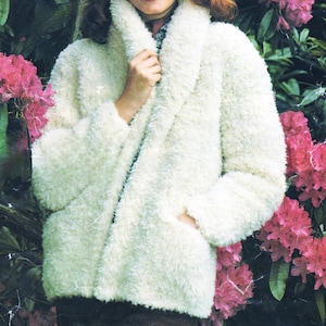 May include: A white fluffy knit jacket with a shawl collar. The jacket is open in the front and has a pocket on the left side.