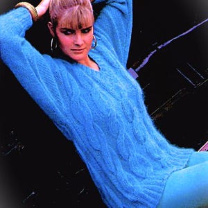 May include: A woman wearing a light blue cable knit sweater with a v-neck. The sweater is soft and fluffy, and the woman is wearing it with a relaxed, casual look.