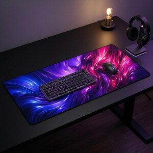May include: A large rectangular mouse pad with a vibrant design of swirling blue and pink colors. A black keyboard and mouse are on the pad. A desk lamp and headphones are also visible on the black desk.