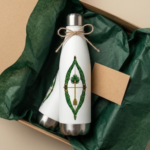 Könnte beinhalten: Weiße isolierte Wasserflasche mit silbernem Deckel und grünem keltischen Knotenmuster mit Kleeblatt und Pfeil. Die Flasche ist mit Bindfaden gebunden und befindet sich in einer Geschenkbox mit grünem Seidenpapier.