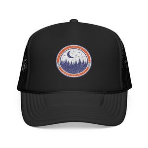 May include: A black trucker hat featuring a circular patch on the front panel. The patch displays a distressed graphic of a dark blue forest silhouette under a crescent moon and stars, framed by a thin white border and a thick orange outer ring.